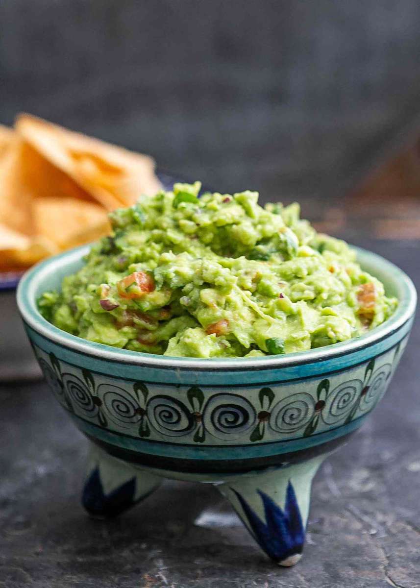 Fresh homemade guacamole served in a traditional Mexican ceramic bowl, with tortilla chips in the background.