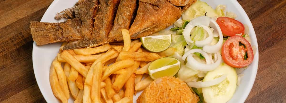 Grilled whole fish with french fries, a hush puppy, cucumber, onion, and tomato