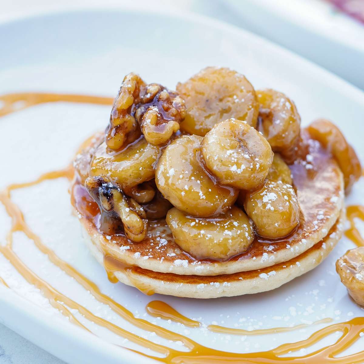 Fluffy pancakes topped with caramelized bananas, walnuts, powdered sugar, and drizzled with caramel sauce.