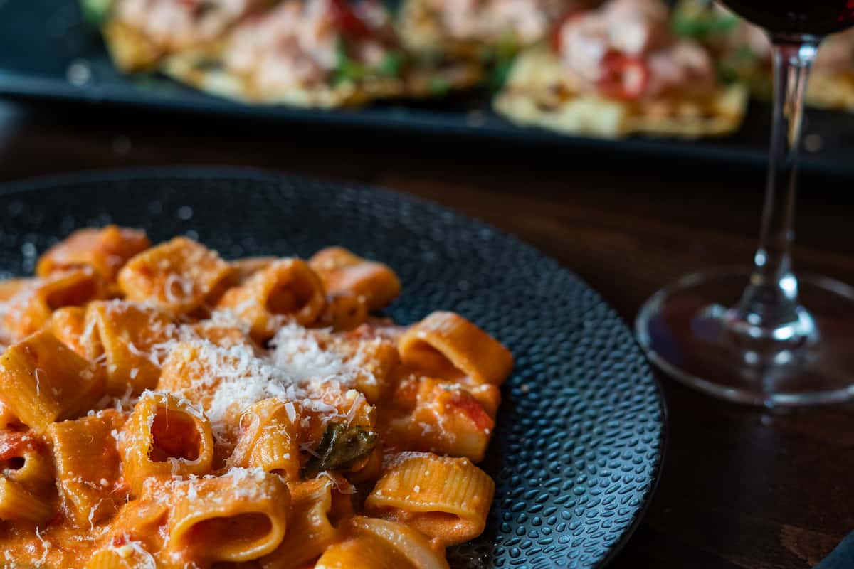 Rigatoni pasta tossed in creamy tomato sauce, topped with grated parmesan and served on a textured black plate.