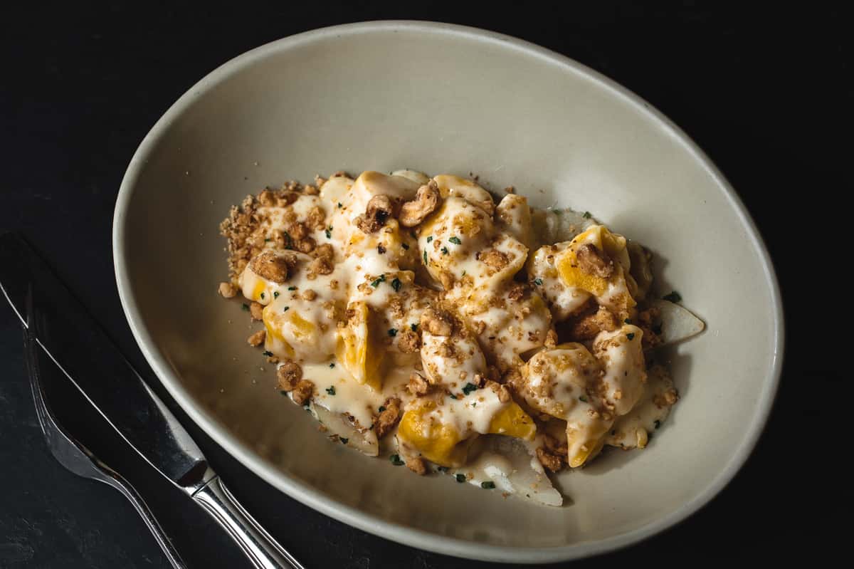 Butternut squash ravioli topped with a creamy sauce, toasted nuts, and fresh herbs in a shallow white bowl.