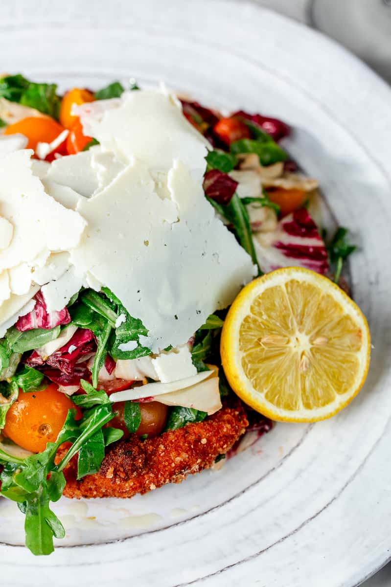 Crispy chicken cutlet topped with arugula, cherry tomatoes, shaved Parmesan, and served with a lemon half.