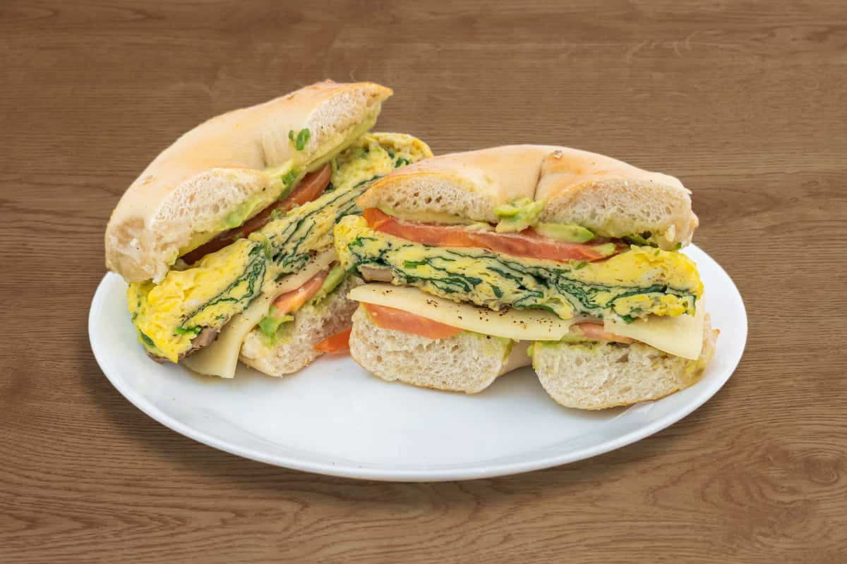 A fresh deli-style sandwich layered with sliced turkey, ham, melted cheese, crisp lettuce, ripe tomato, and fluffy eggs on multigrain bread. Cut into halves and served on a white plate, this hearty sandwich is packed with fresh ingredients, making it a satisfying choice for breakfast or lunch.