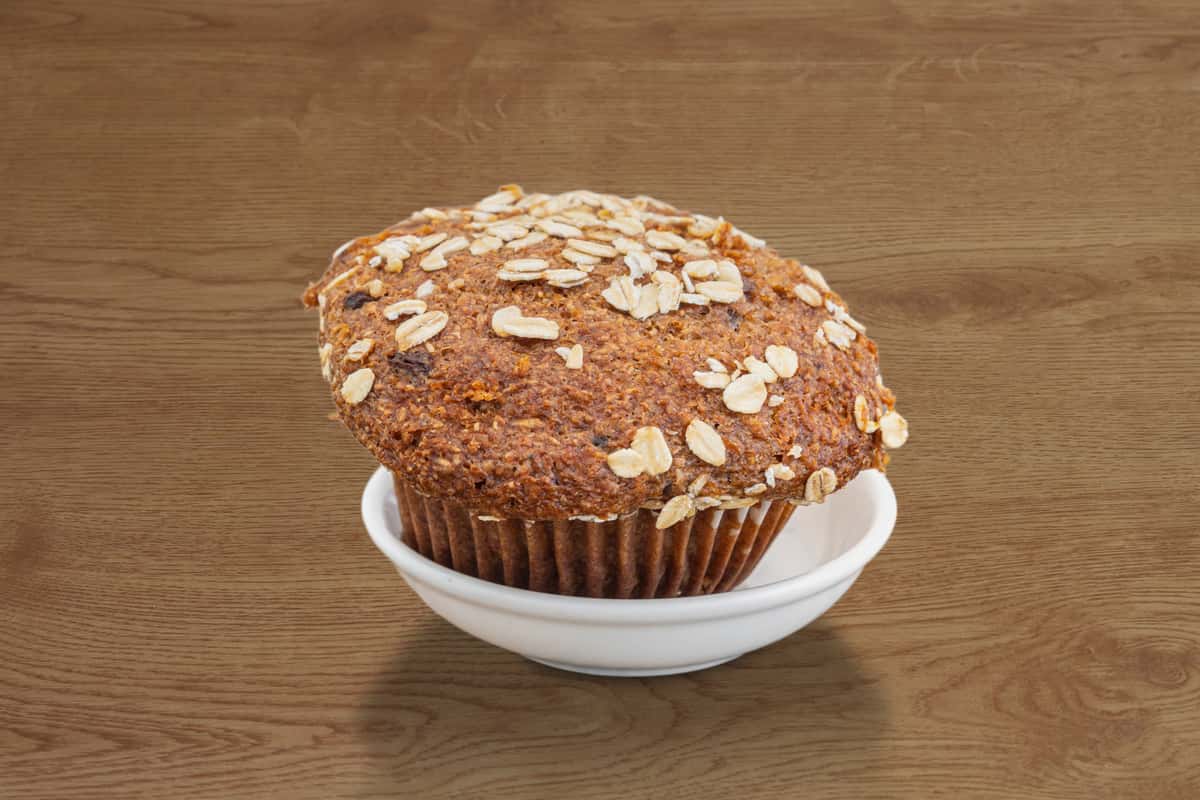 A freshly baked bakery-style muffin topped with sliced almonds and a light dusting of sugar. Served in a white ramekin, the golden-brown muffin has a soft, fluffy texture and a wholesome appearance, making it a delicious choice for breakfast, brunch, or a midday treat.