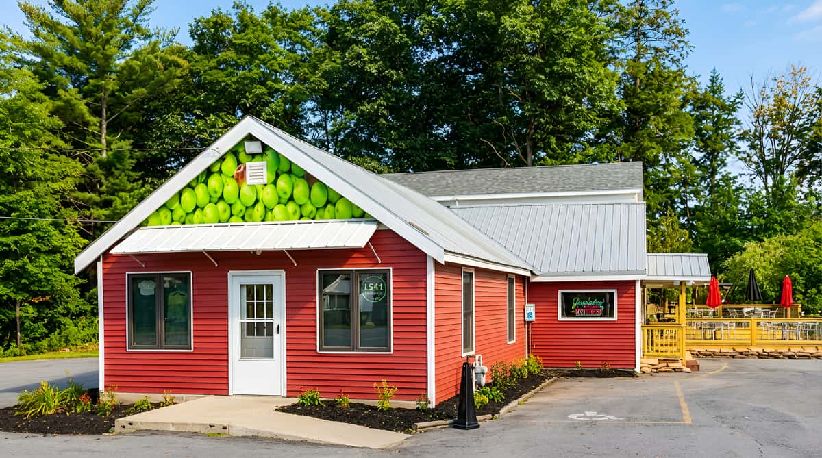 Red building with green apple mural on front gable, attached to a gray roof, with an outdoor patio area.