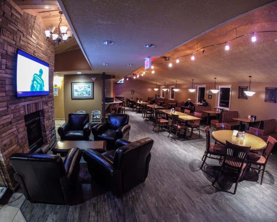 Lounge room with fireplace, television, leather chairs adjacent to dining tables and booths.