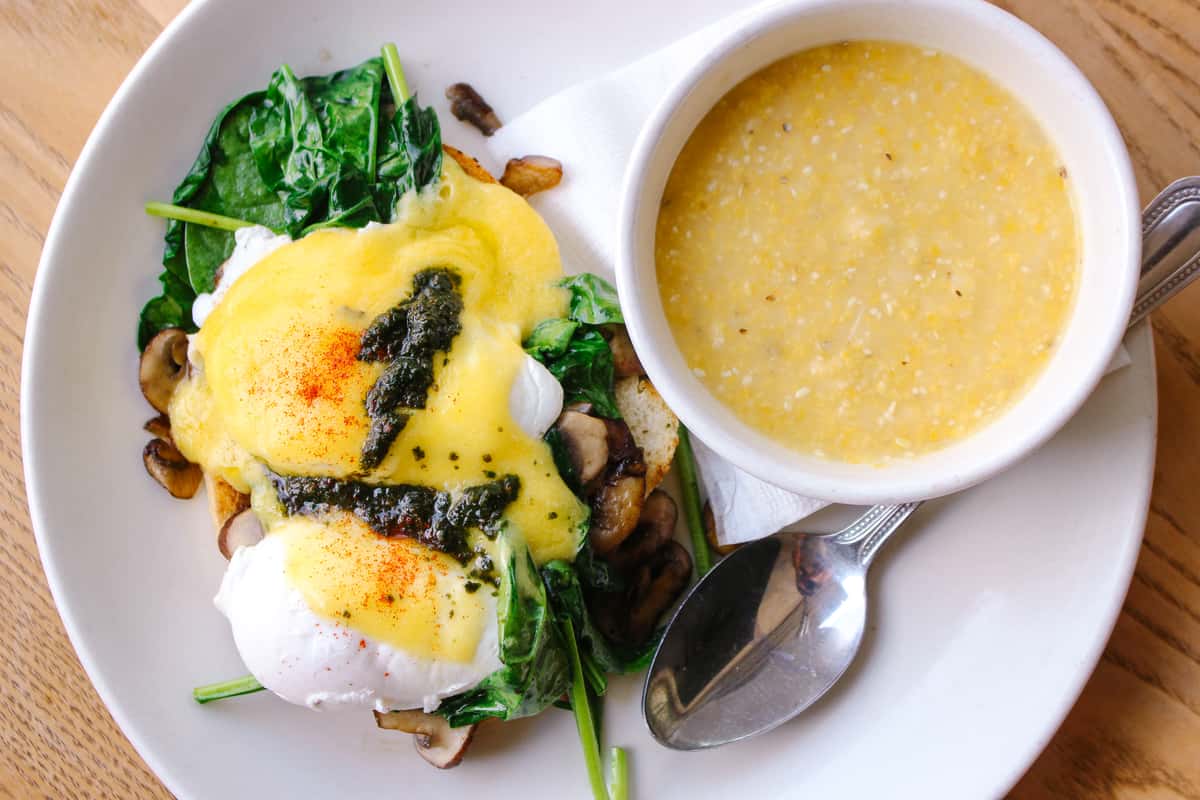 Eggs Benedict with sautéed spinach, mushrooms, hollandaise sauce, and pesto, served with a side of creamy grits.