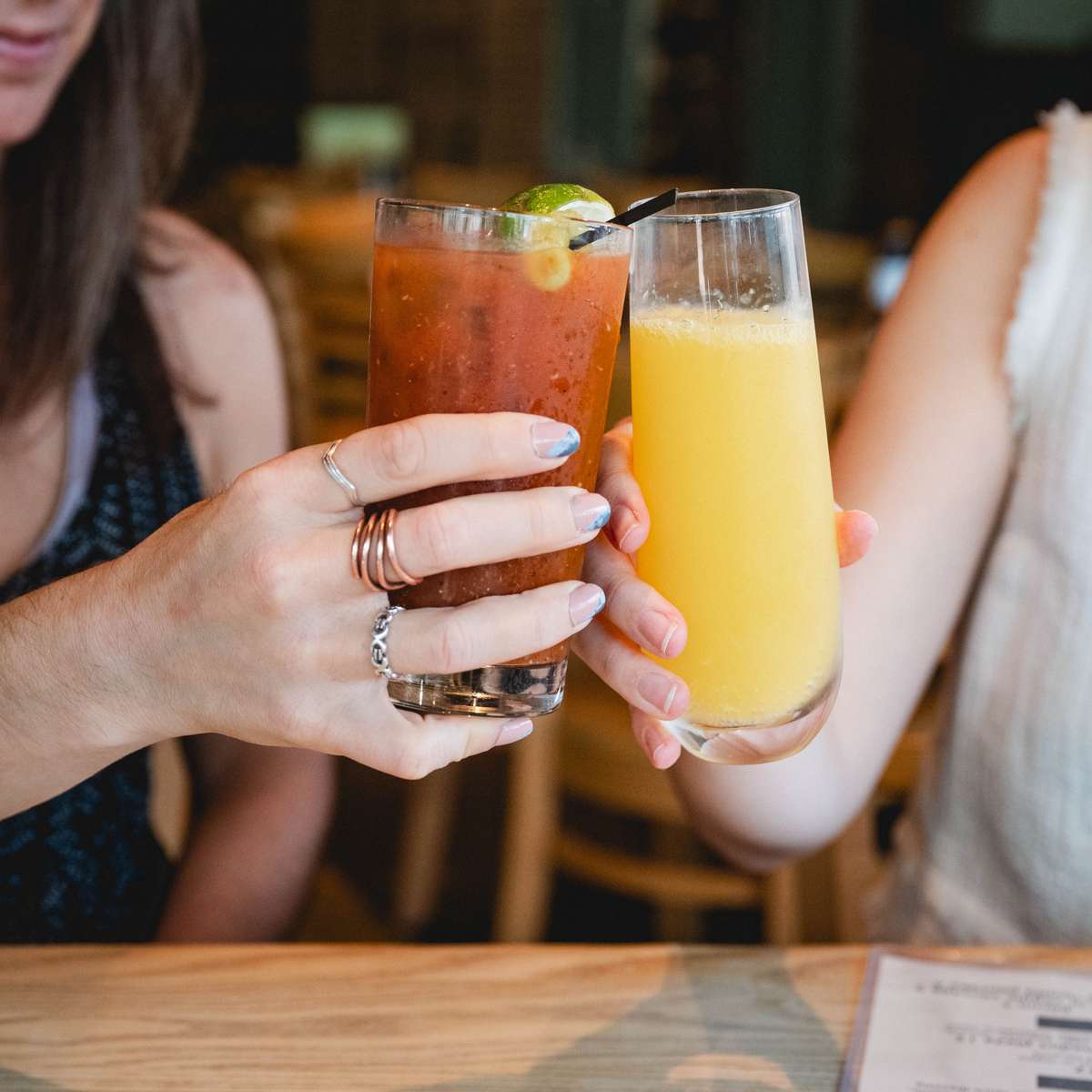 Two people clinking glasses, one holding a Bloody Mary with lime and the other a mimosa filled with fresh orange juice.
