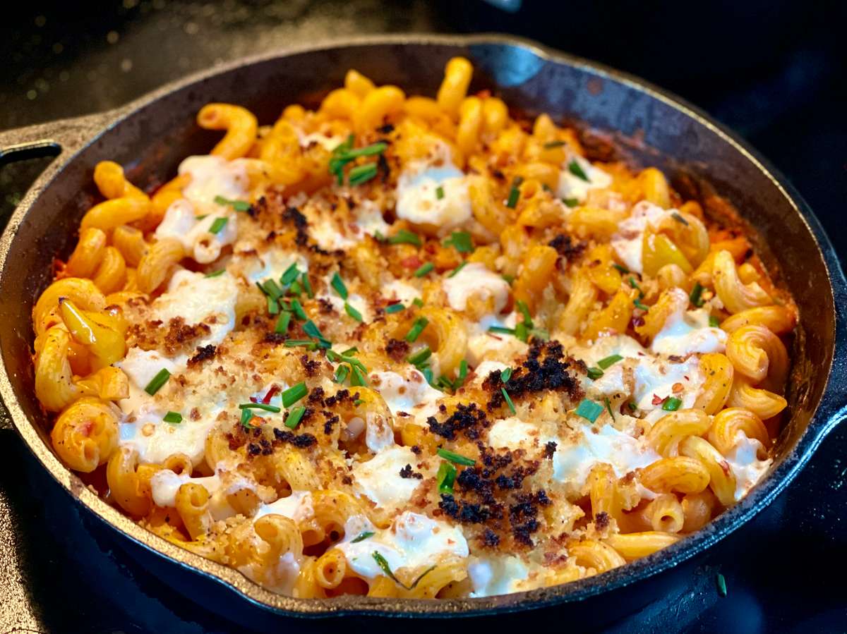 Creamy baked mac and cheese topped with melted cheese, crispy breadcrumbs, and fresh herbs, served in a cast iron skillet—classic comfort food with a rich, cheesy texture.