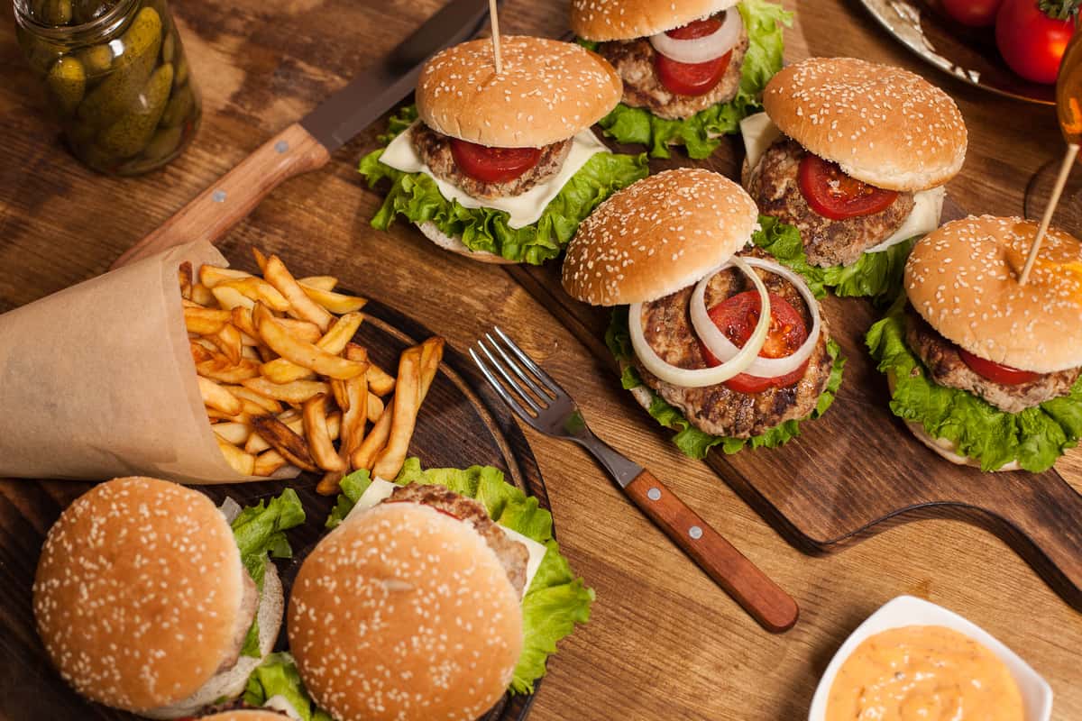 Several gourmet burgers with fries and pickles are arranged on a wooden board, showcasing a delicious meal at Spot Gourmet Burgers.