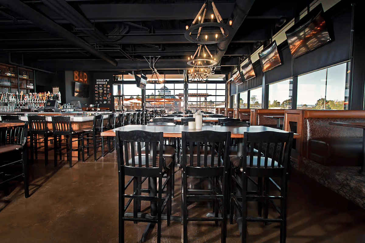 Modern restaurant bar and dining area with communal seating, televisions, and an open layout designed for sports viewing and casual dining.