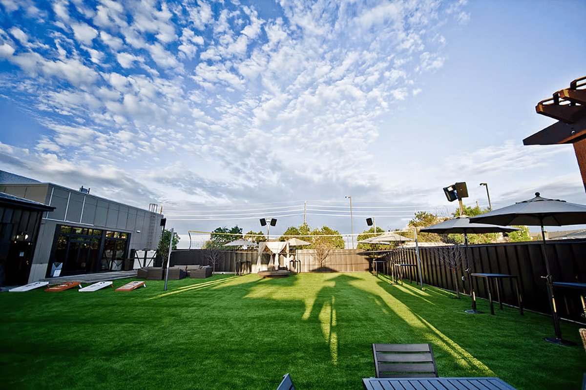 Expansive outdoor lawn venue with yard games, patio seating, and open green space for events, parties, and community gatherings.