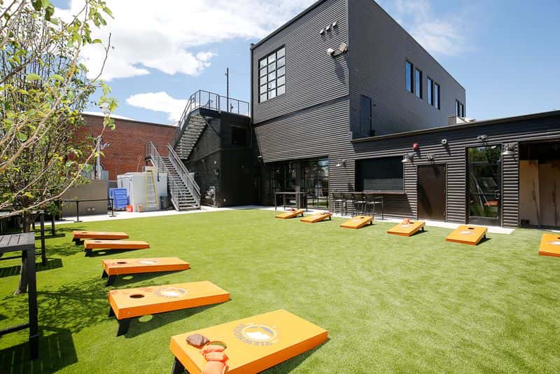Outdoor lawn venue with cornhole boards, artificial turf, and open event space for games, private parties, and social gatherings.