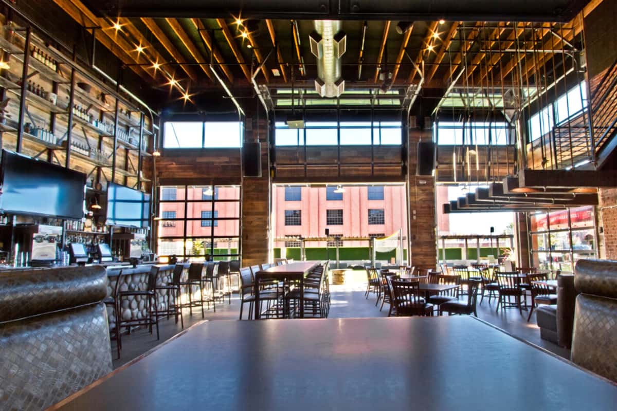 Open-concept restaurant interior featuring floor-to-ceiling windows, industrial design, bar seating, and a bright social dining atmosphere.