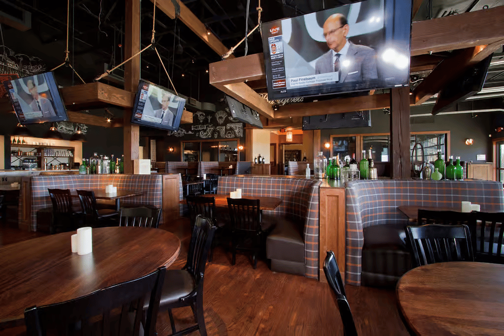 Sports bar interior with booth seating, multiple televisions, wood finishes, and a lively atmosphere for watching games and enjoying drinks.