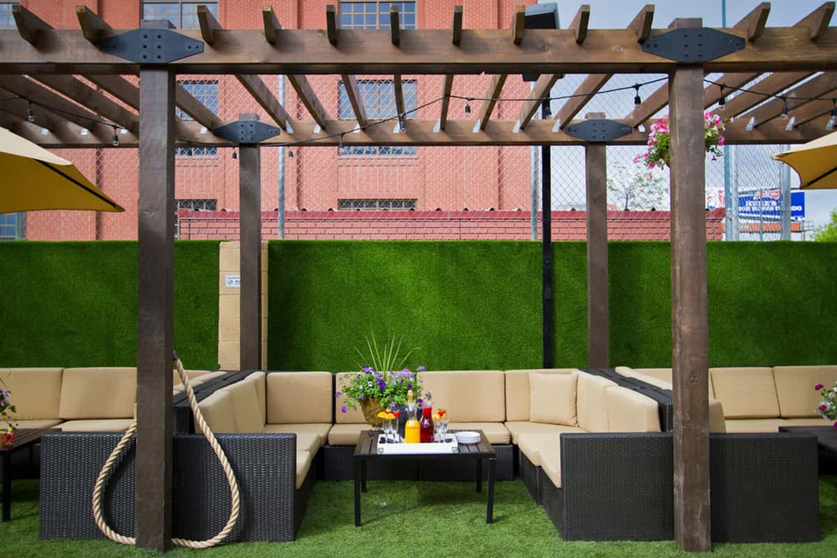 Private outdoor lounge cabana with cushioned sectional seating, pergola shade, and cocktail service in a landscaped patio setting.