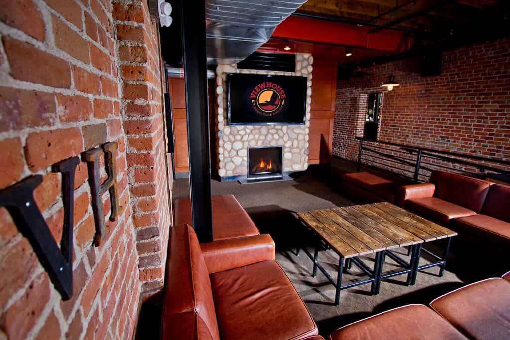 Cozy lounge area with leather seating, fireplace, exposed brick accents, and a relaxed gathering space inside a modern restaurant.
