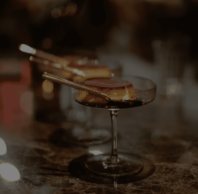 Craft cocktail in a coupe glass with garnish on a marble bar counter, stylish drink presentation in an upscale restaurant or lounge.
