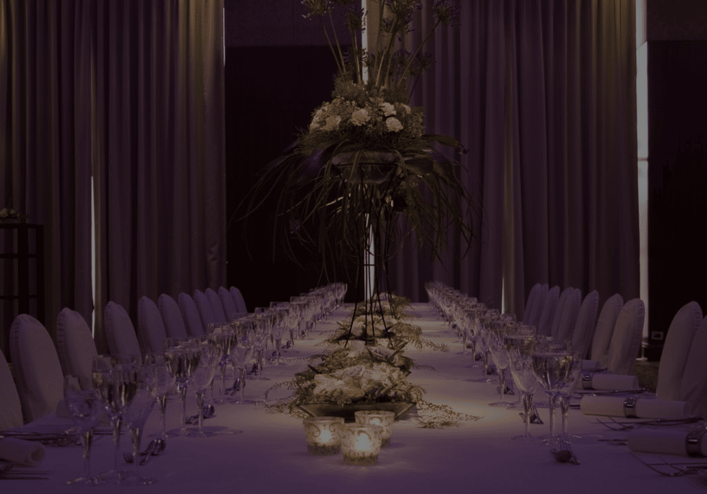 Elegant banquet dining table setup with white linens, crystal glassware, candlelight, and tall floral centerpieces, creating a luxurious restaurant or wedding reception atmosphere