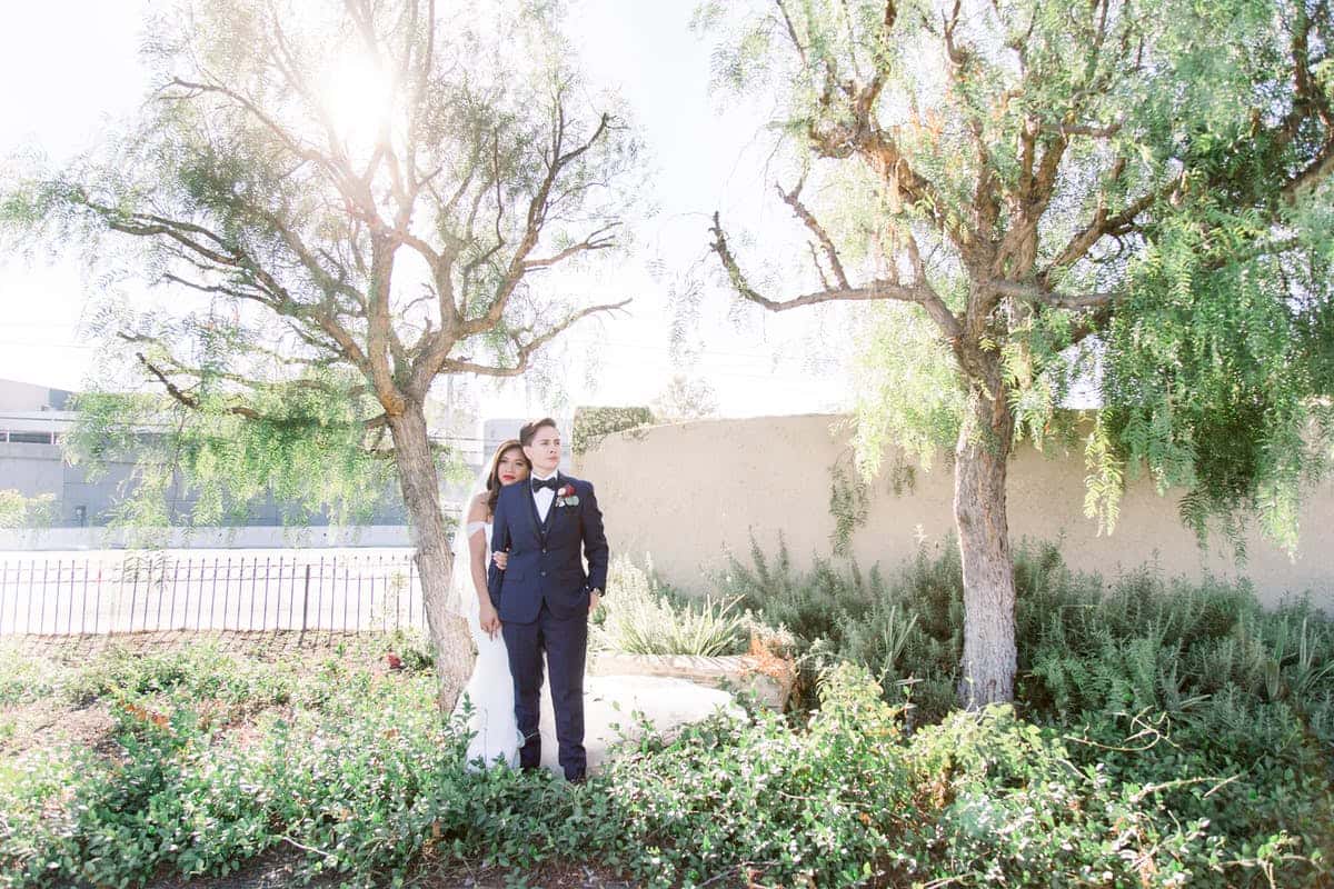 Bride and groom standing together in a sunlit garden setting during an elegant outdoor wedding portrait session