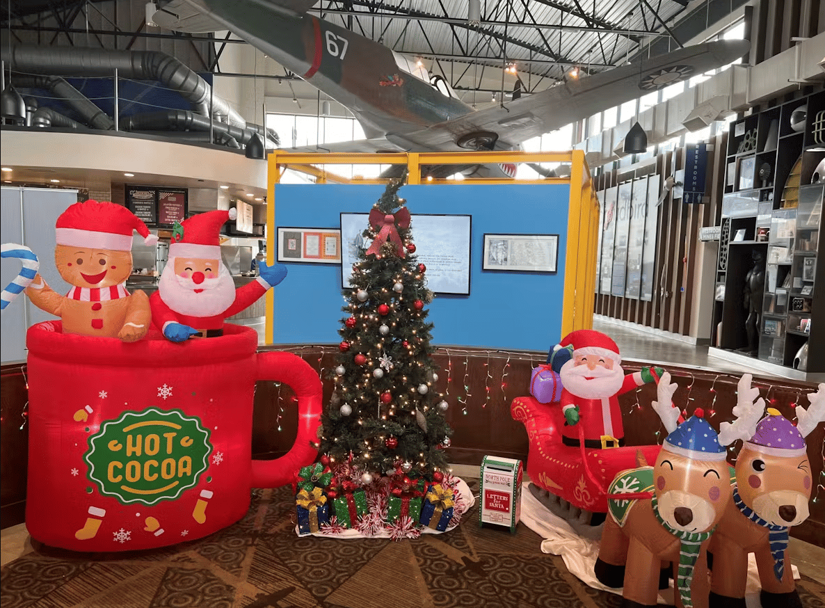 Festive holiday display with Christmas tree, inflatable Santa decorations, and aviation-themed décor inside a modern restaurant and event venue