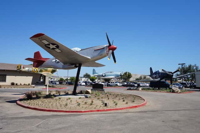 Vintage military aircraft display outside an aviation-themed venue featuring restored warplanes and outdoor museum exhibits under a clear blue sky