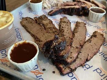 Sliced smoked brisket platter with barbecue sauce and classic Southern sides served on a butcher paper-lined tray at a modern barbecue restaurant