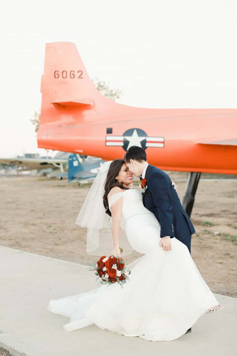 Bride and groom posing beside a vintage aircraft at an aviation-themed wedding venue with romantic outdoor scenery
