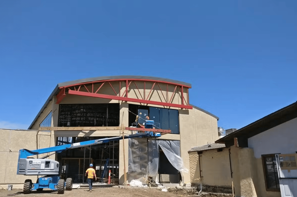 Exterior view of The Proud Bird aviation-themed venue during renovation with construction lifts and modern industrial architecture under a clear blue sky