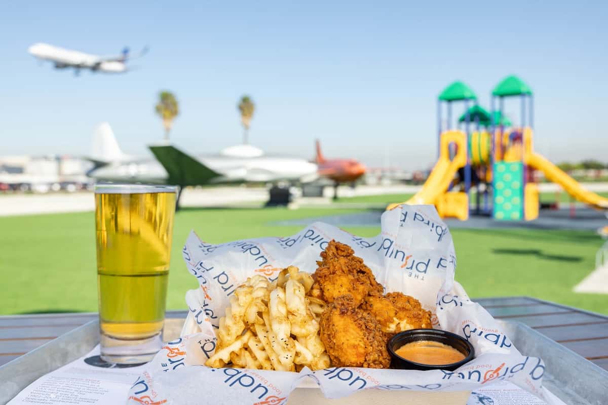 A tray of chicken, fries and beer with planes and playground equipment in the background