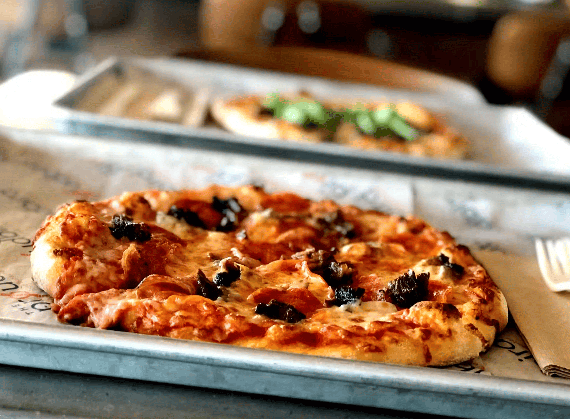 Personal pepperoni and sausage pizza with melted mozzarella served on a metal tray at a casual modern pizzeria