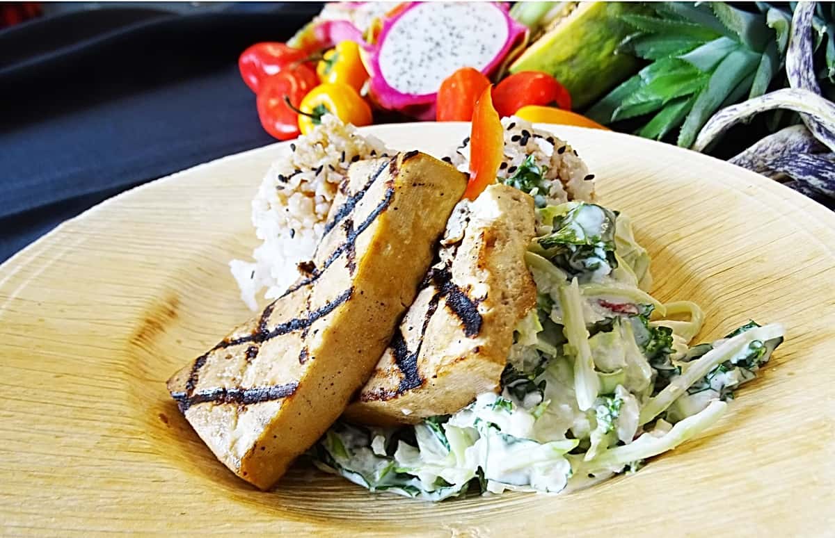 Grilled tofu slabs with sear marks served over creamy cabbage slaw, paired with brown rice and tropical fruits – a clean and protein-rich vegetarian Hawaiian option.