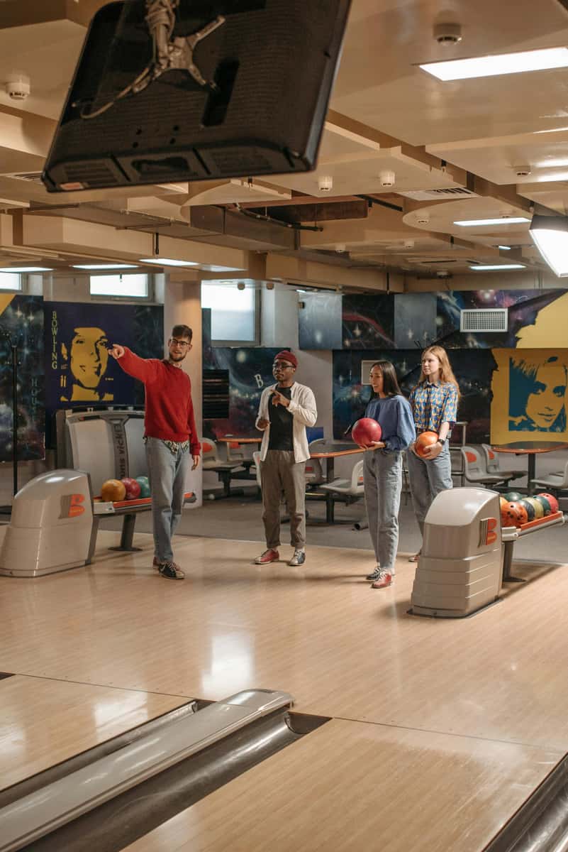 Four friends are ready to bowl, each holding a bowling ball, at the lanes of The Social Duck.