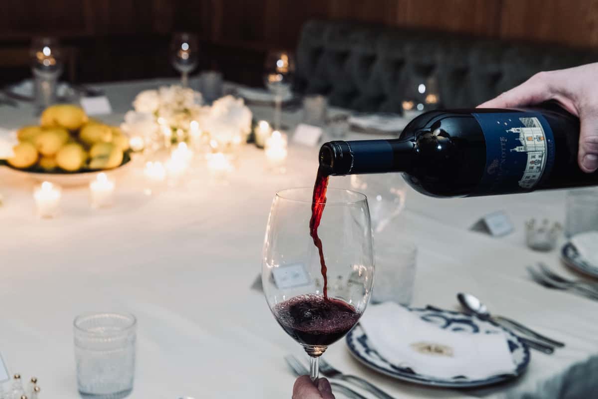 Red wine poured into glass at elegantly set table with candles and floral centerpiece in background