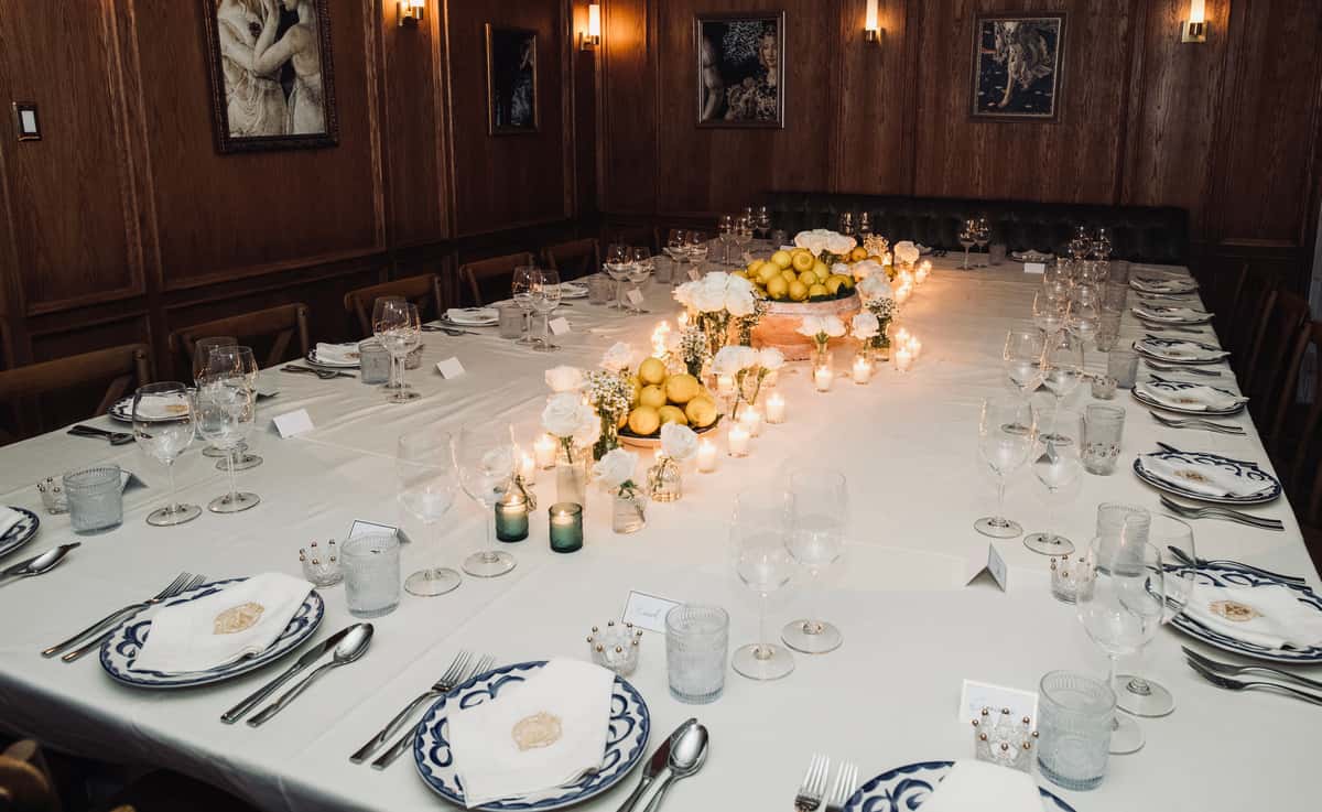 Elegant long dining table set with white linens, candles, lemons, and floral centerpieces in wood-paneled room