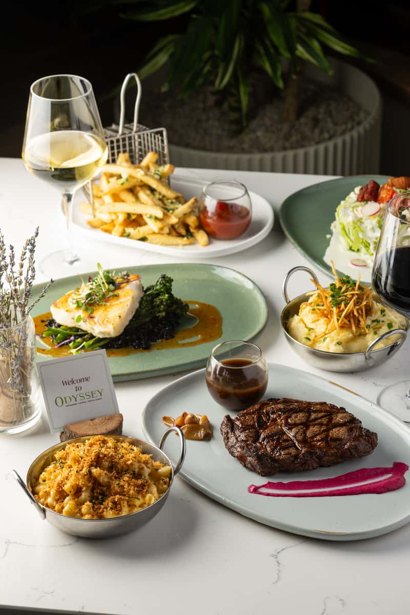 a table with steak and seafood on it with a sign that says Welcome to Odyssy