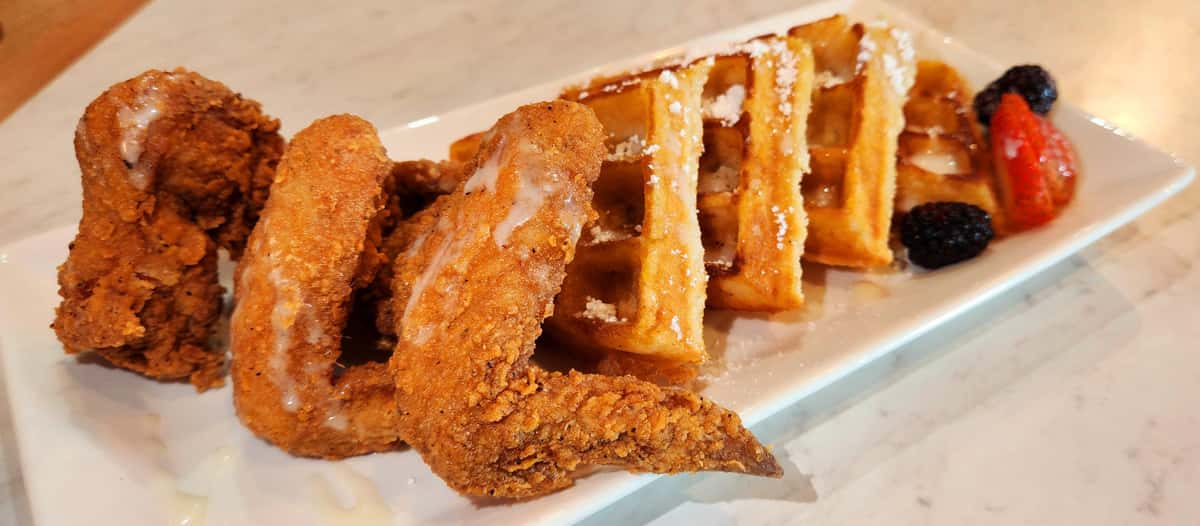 Crispy Southern-style fried chicken wings served with golden Belgian waffles, drizzled with sweet icing and paired with fresh blackberries and strawberries.