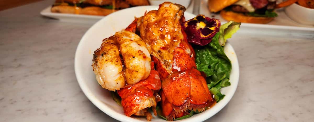Succulent grilled lobster tails glazed in savory butter sauce, served over a bed of fresh greens and garnished with a vibrant edible flower.