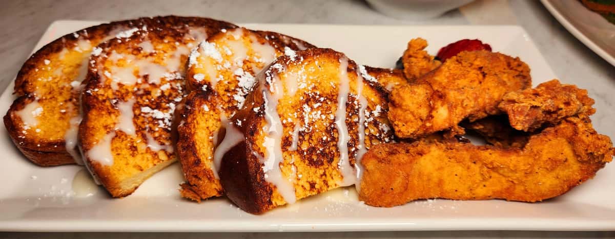 Crispy golden fried chicken tenders paired with thick-cut French toast slices, drizzled with icing and dusted with powdered sugar, creating a sweet and savory brunch favorite.