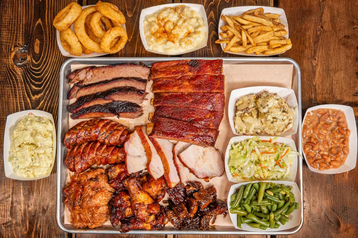 Group shot of food with ribs and wings plus side like onion rings, fries and more