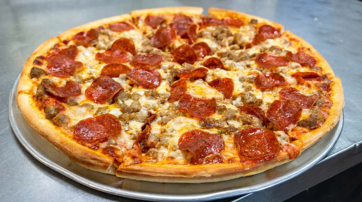 Pepperoni and sausage pizza with melted cheese on a metal pan.