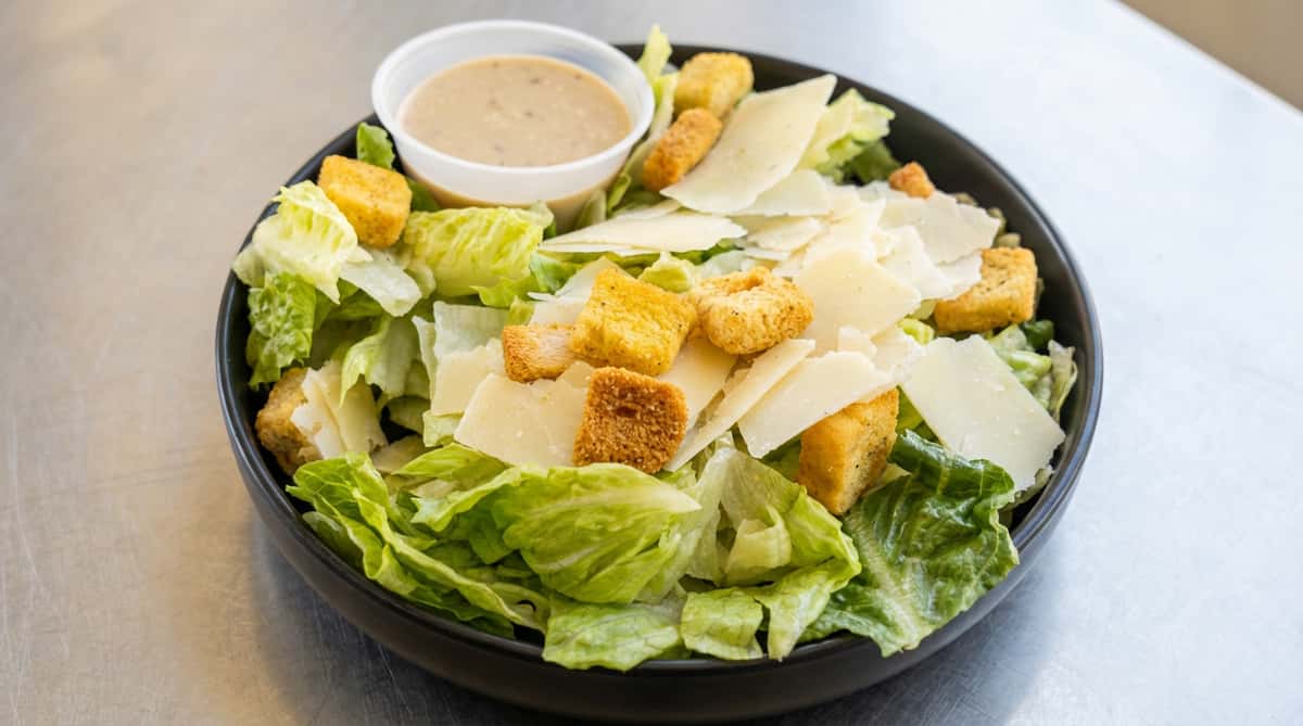 Caesar salad with romaine lettuce, Parmesan shavings, croutons, and a cup of dressing.