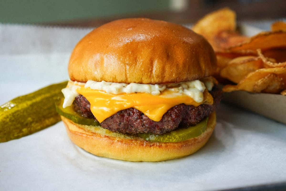 Cheeseburger with cheddar, pickles, and creamy sauce on a toasted bun, served with a pickle spear and kettle-cooked chips.