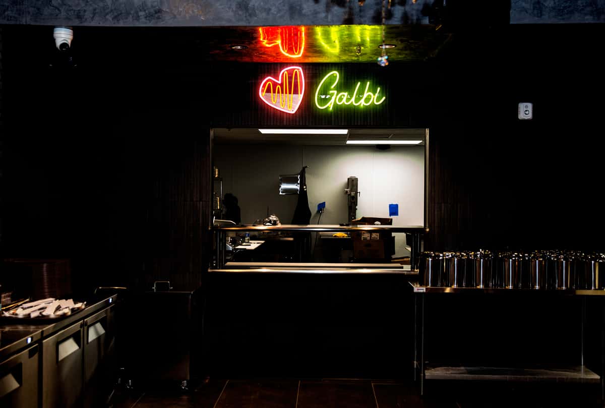 Restaurant kitchen window with neon sign reading "♥ Galbi" in red and green above the serving area.