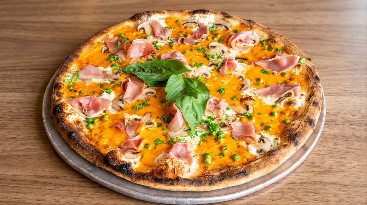 Pizza topped with prosciutto, basil, and melted cheese on a wooden table.