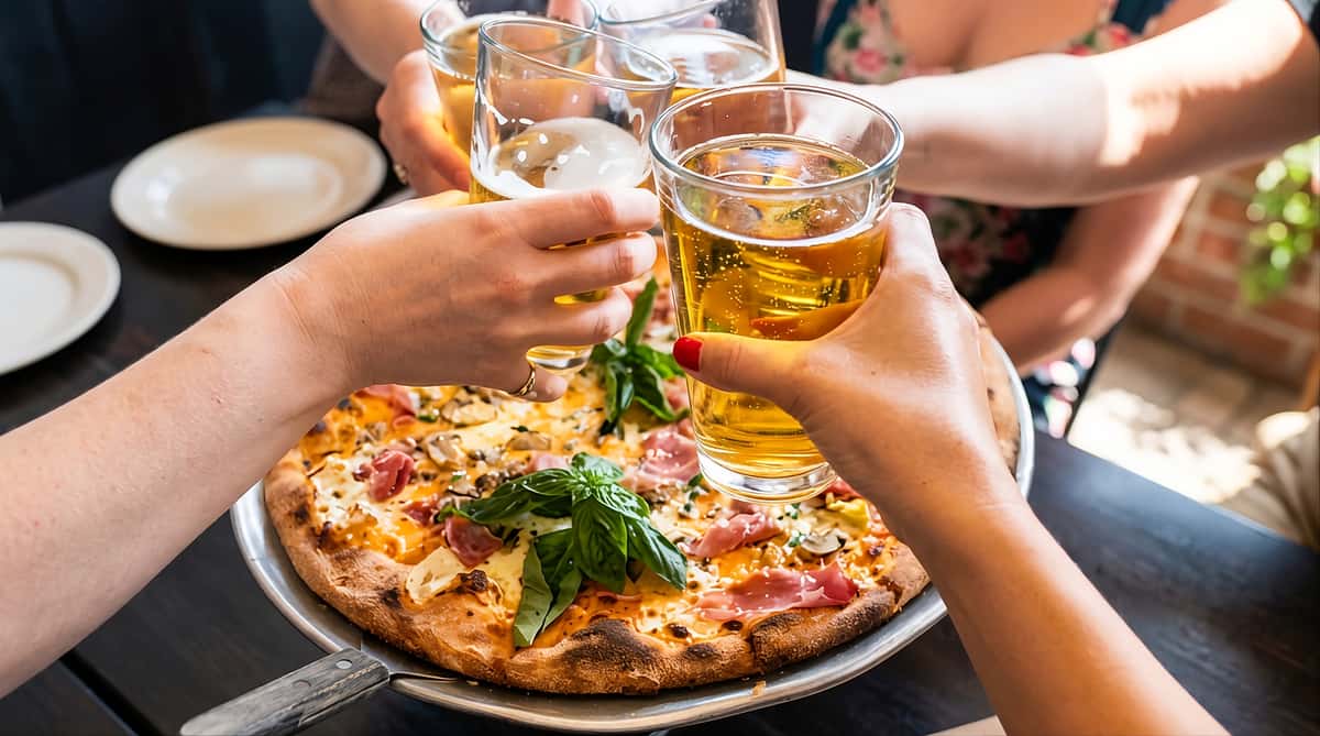 Group of people clinking glasses over a pizza on a restaurant table.
