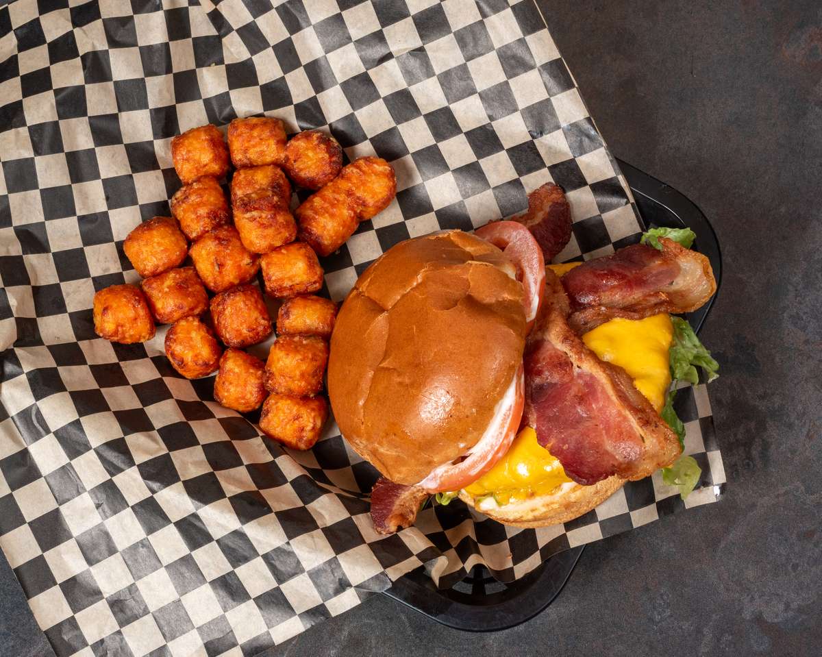 Bacon cheeseburger with cheddar cheese, lettuce, tomato, and sweet potato tots served on the side.