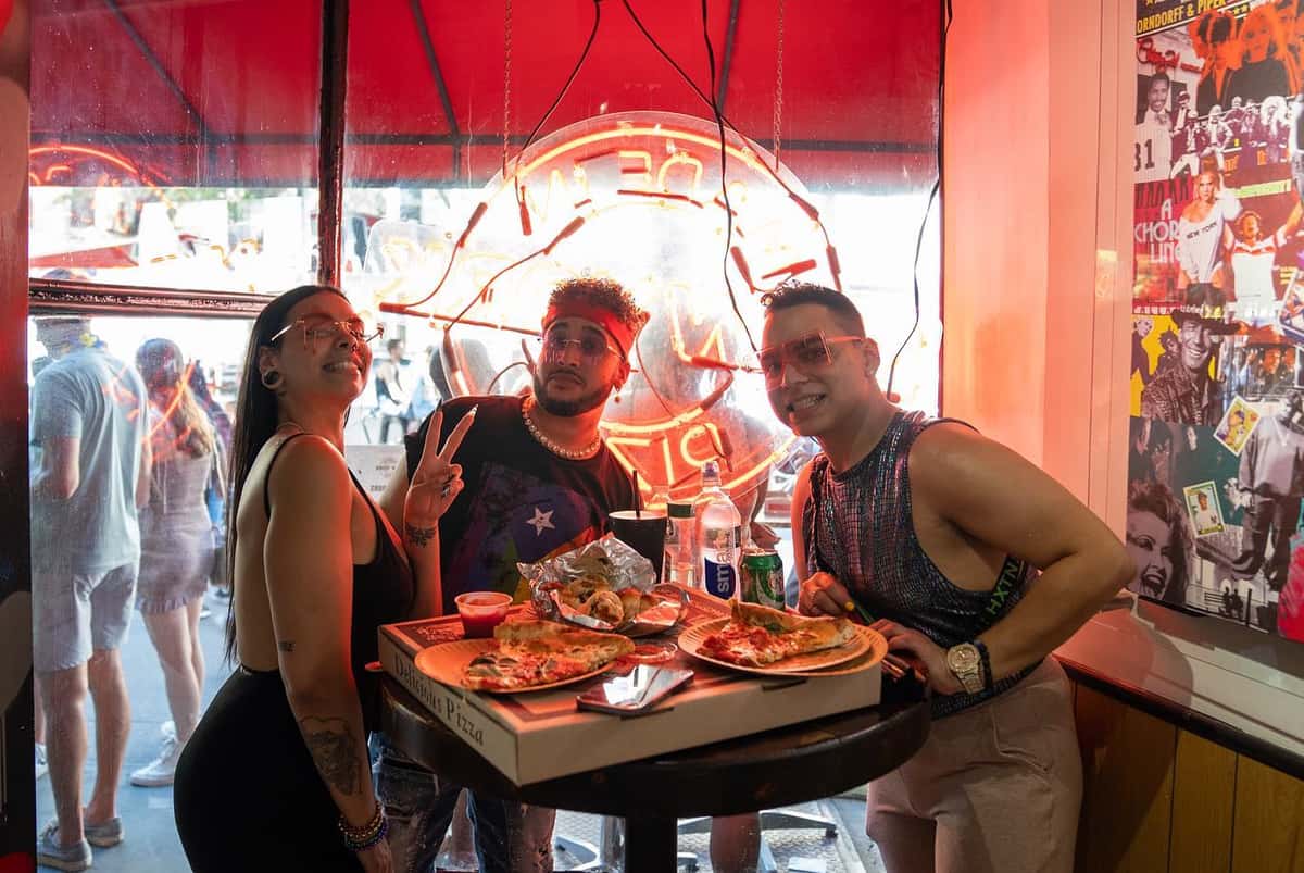 group of friends dining at a restaurant table with pizza and drinks in a lively neon-lit setting