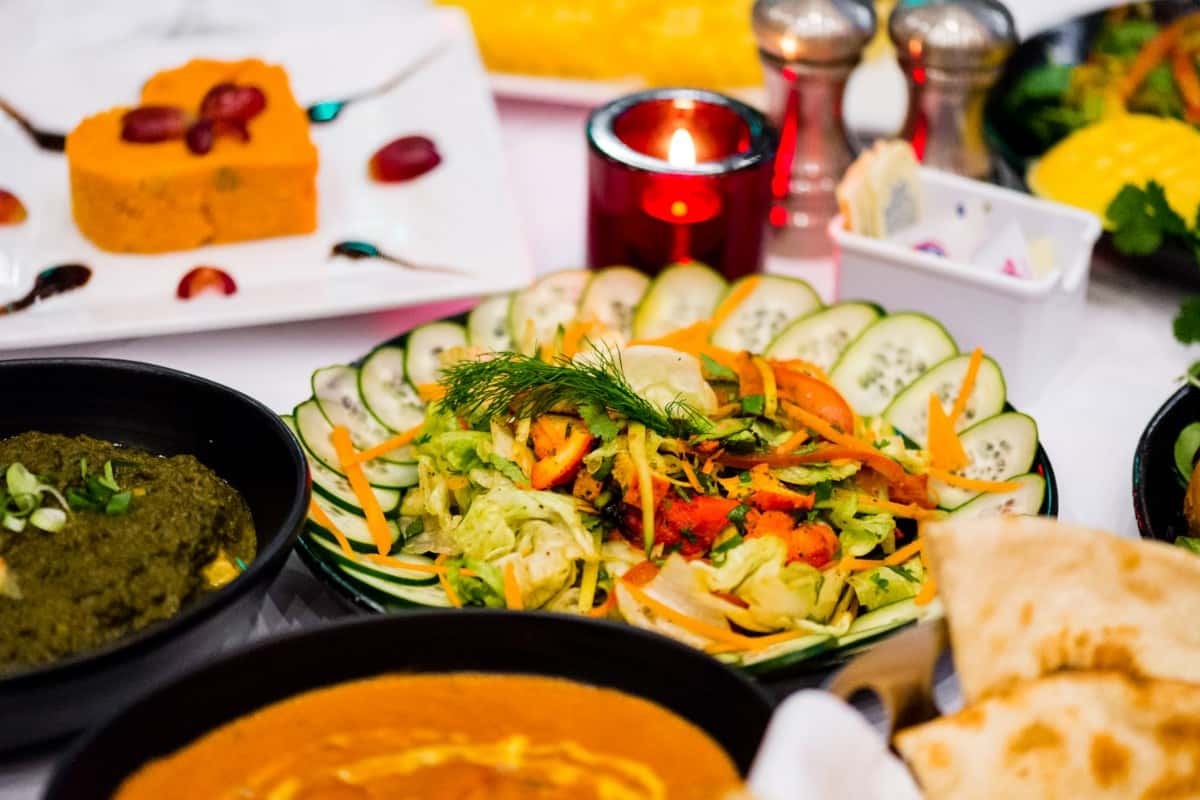 Colorful Indian salad with shredded carrots, lettuce, cucumber slices, and fresh herbs surrounded by curry, saag, and naan bread
