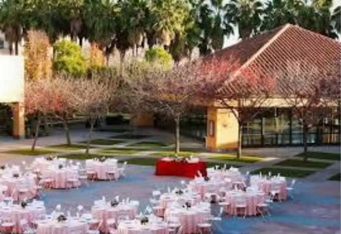 Outdoor garden reception setup with round dining tables, floral decor, and scenic waterfront event ambiance